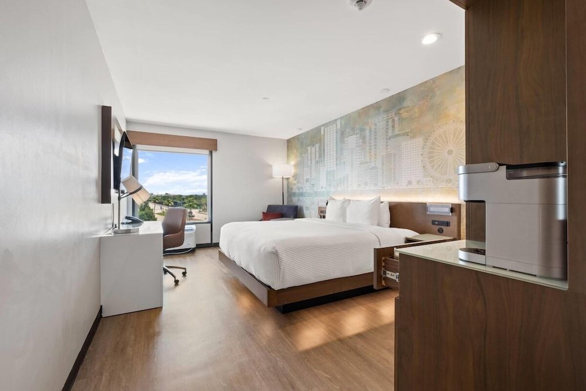 Een moderne hotelkamer met een bed, bureau en uitzicht op de stad.