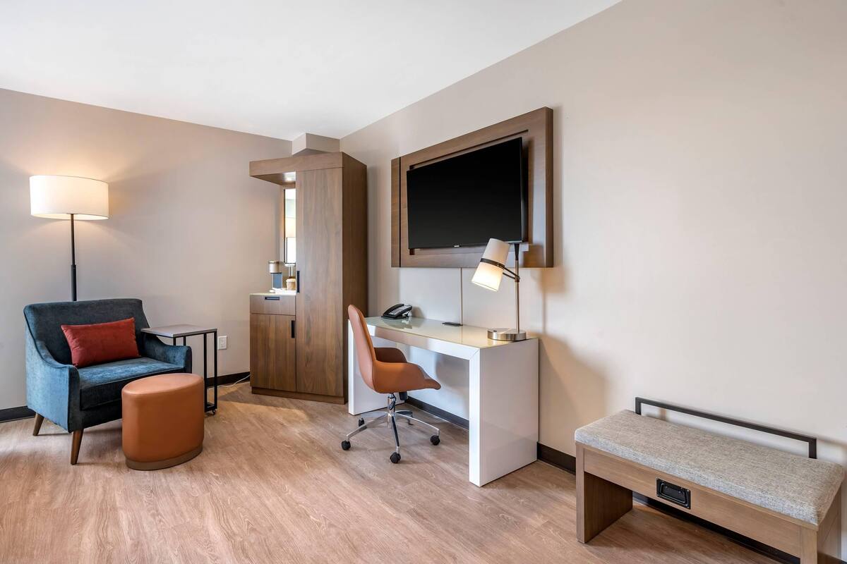 Una habitación de hotel con escritorio, silla, reposapiés y banca.