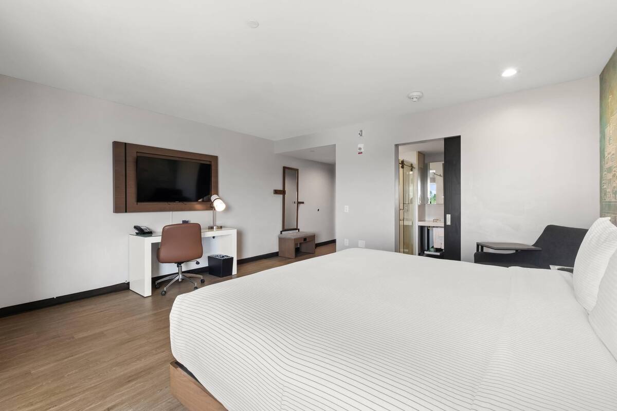 Una habitación de hotel con una cama grande, un escritorio con silla, un televisor y una puerta que da a otra habitación.