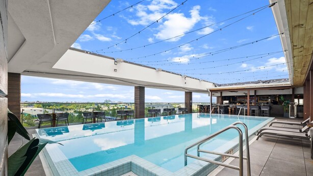Una piscina infinita al aire libre con una vista despejada del paisaje urbano, rodeada de sillones de descanso y una zona de bar.