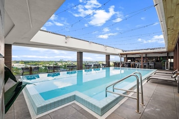A modern hotel room with a wooden desk, a flat-screen TV mounted on the wall, a large window with a view, and a walk-in closet with hanging space. at Cambria Hotel Orlando Universal Blvd