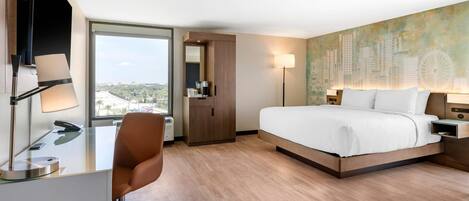A modern hotel room with a large bed, a desk with a chair, a coffee machine, and a cityscape view through the window.