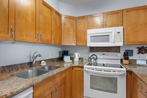 A kitchen with wooden cabinets, a stainless steel sink, a microwave, a stove, and a coffee maker.