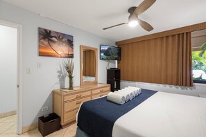 Un dormitorio con cama, cómoda, televisor y ventilador de techo.