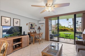 Una sala de estar con televisor, muebles de madera y un balcón con vista a palmeras.