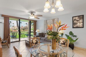 Ein modernes Wohnzimmer mit Glastisch, bequemen Sitzmöglichkeiten, Deckenventilator und Blick ins Freie.