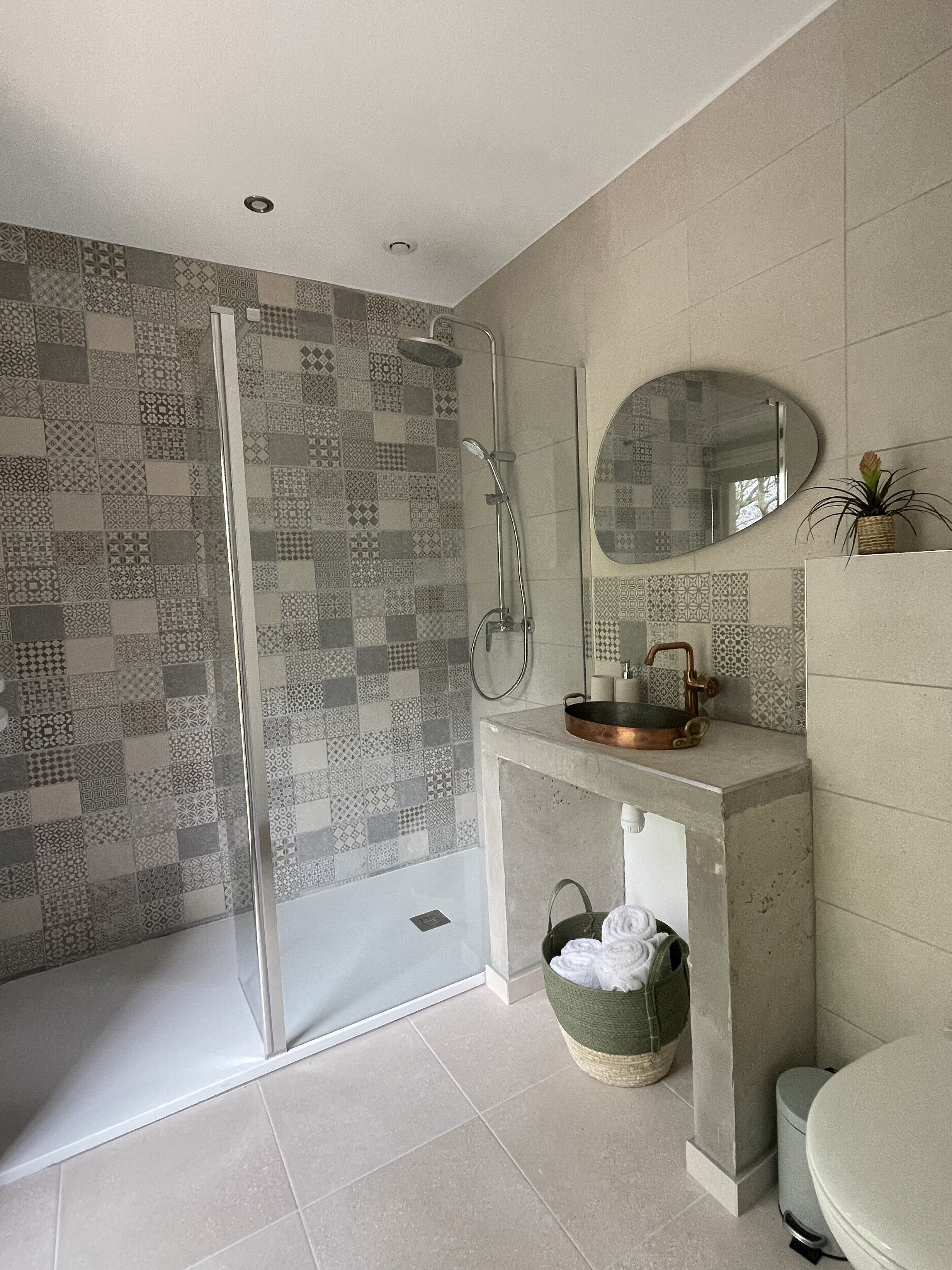 A modern bathroom with a shower, a sink with a copper basin, a mirror, and a toilet.