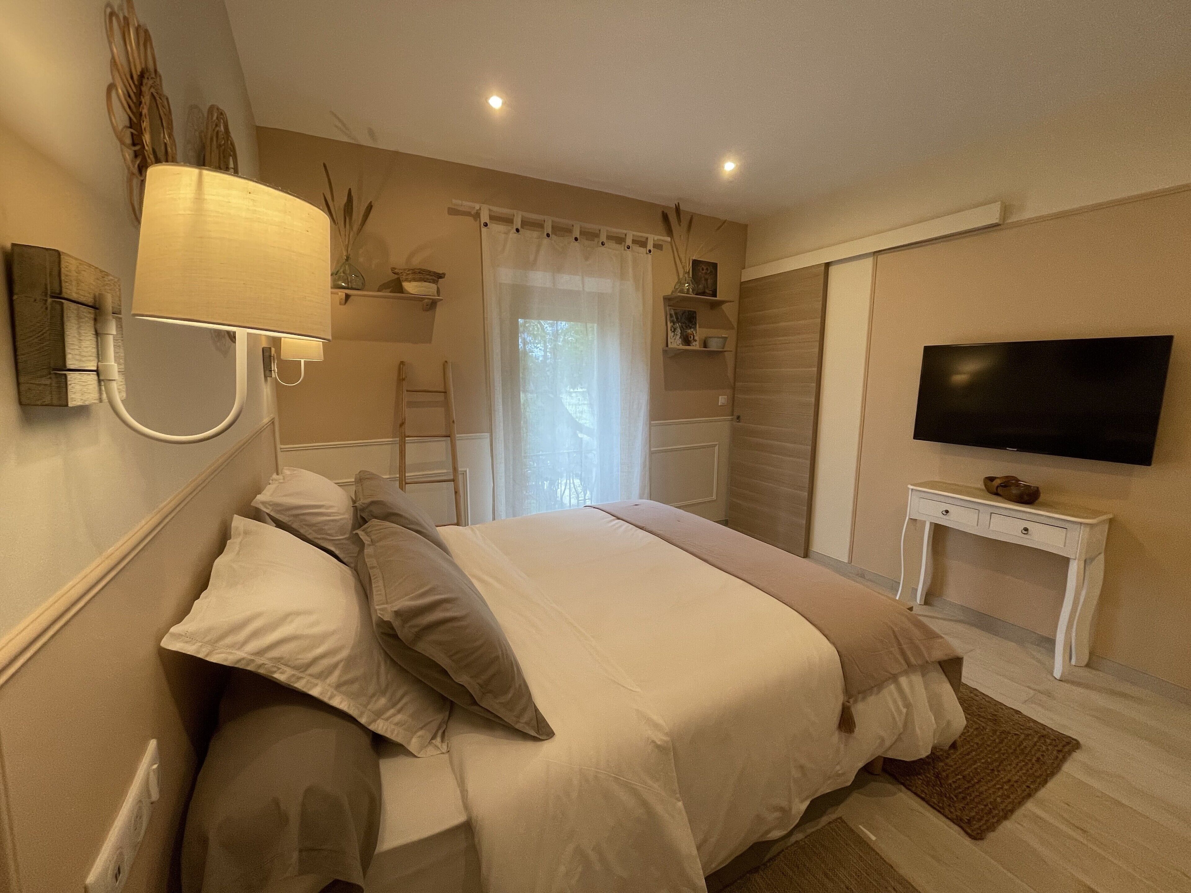 A bedroom with a bed, bedside lamp, TV, and a small table.