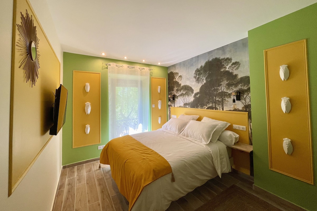 A bedroom with a bed, a television, a painting, and a door with a view.