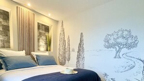 Un dormitorio moderno con cama, mesita de noche, un mural en la pared y un taburete pequeño.