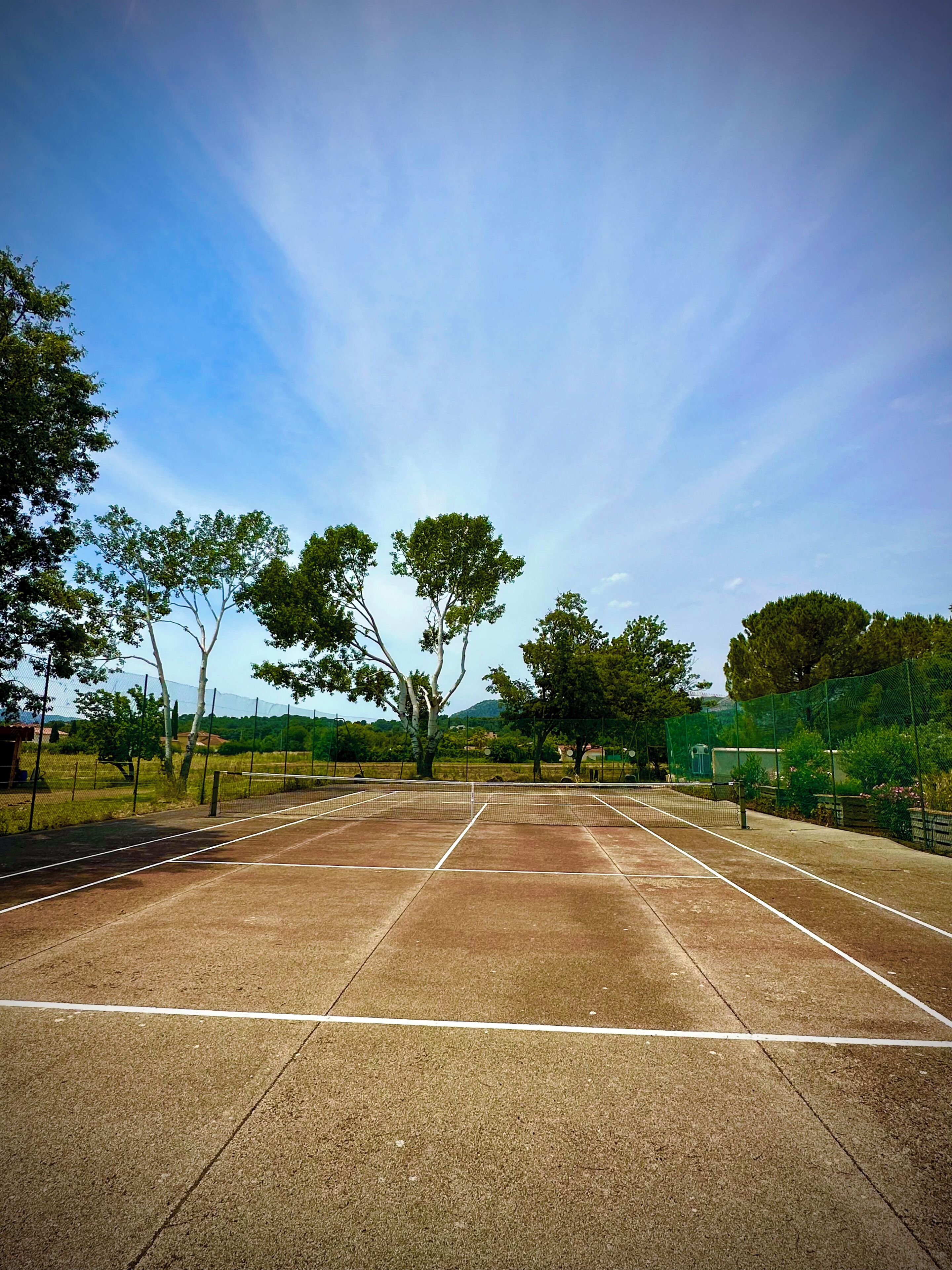 Un court de tennis avec un filet, entouré d’arbres et sous un ciel dégagé.