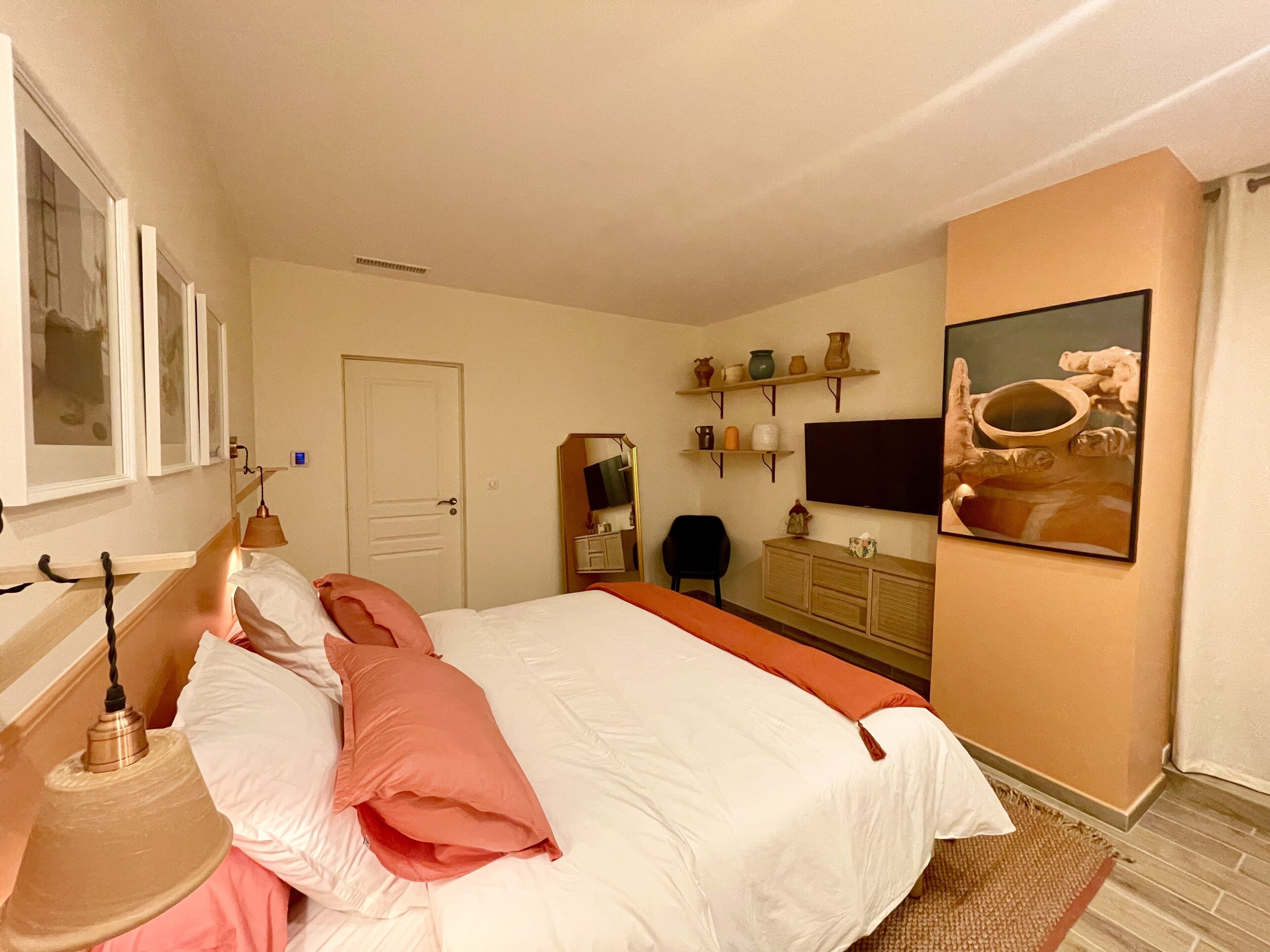 A bedroom with a bed, a dresser, a chair, a television, and shelves with decorative items.
