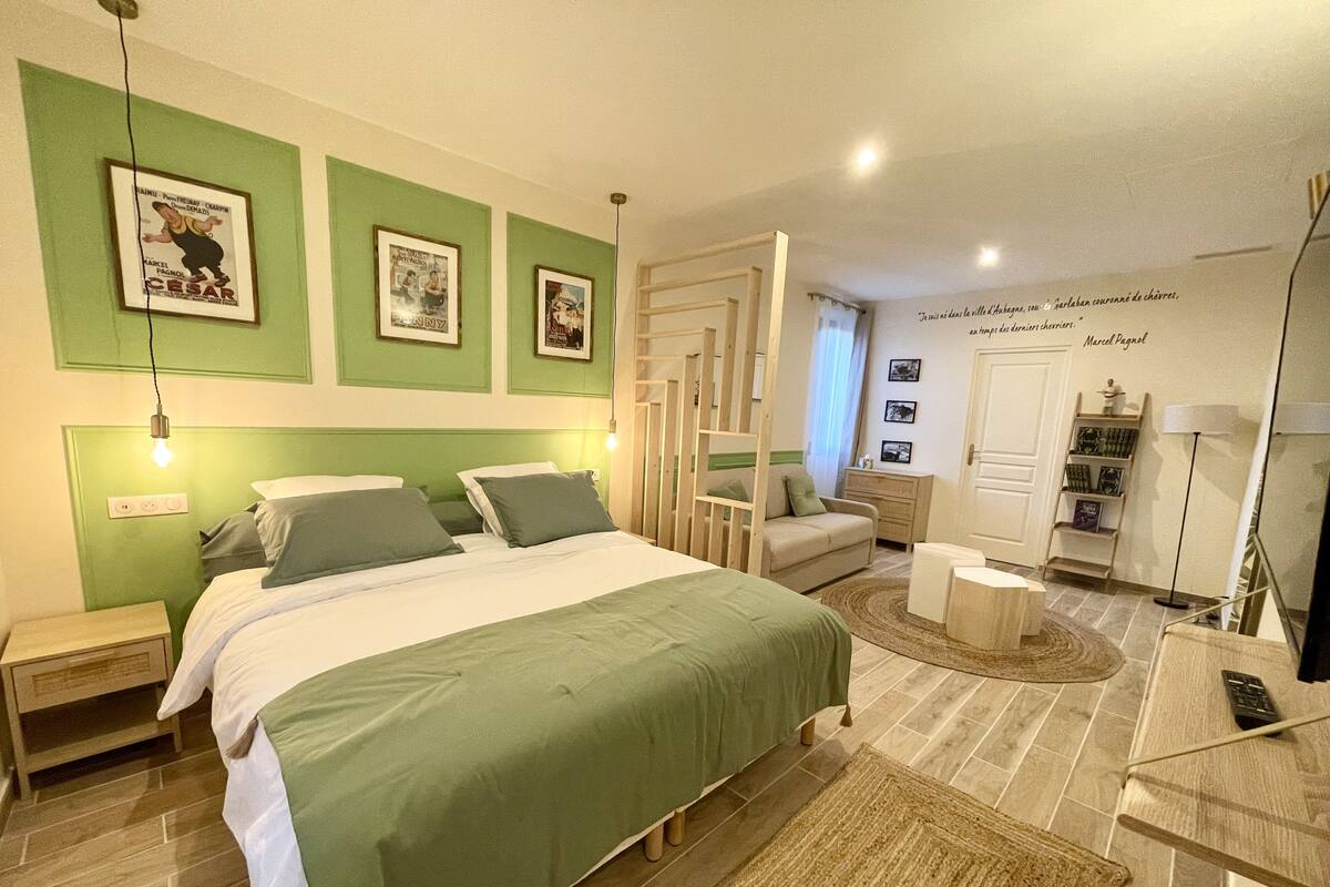 A bedroom with a large bed, a bedside table, a nightstand, a dresser, a mirror, and a wall with framed pictures.