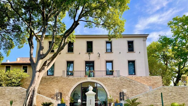 Un edificio con fachada de piedra, una entrada central en arco y una fuente al frente.