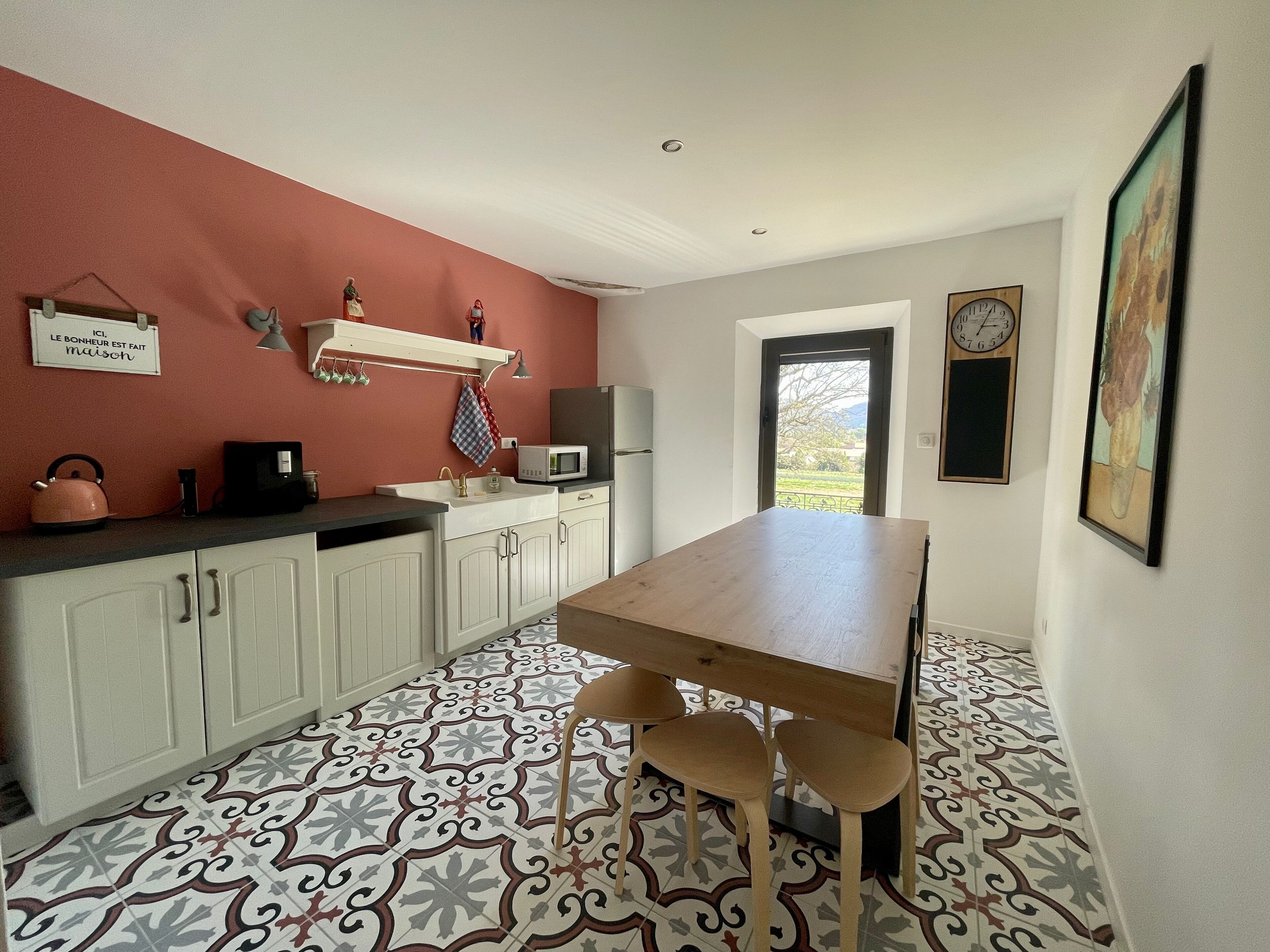 A compact kitchen with white cabinets, a wooden table, and a patterned floor.