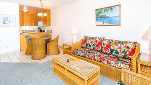 A living room with a sofa, coffee table, wicker chairs, a ceiling fan, and a kitchen in the background. - Casual Kihei! WiFi, AC, Ceiling Fans, Laundry, Kitchen, Lanai, TV–Kamaole Sands 8209 (KIHEI)