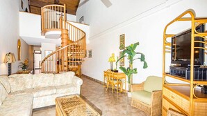 A spacious living area with a wooden staircase, a sofa, a coffee table, and a television on a wooden stand.