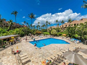 A swimming pool area with lounge chairs and umbrellas, surrounded by palm trees and hotel buildings. - 2-Level Condo w/Kitchen - Kamaole Sands 5407 (KIHEI)