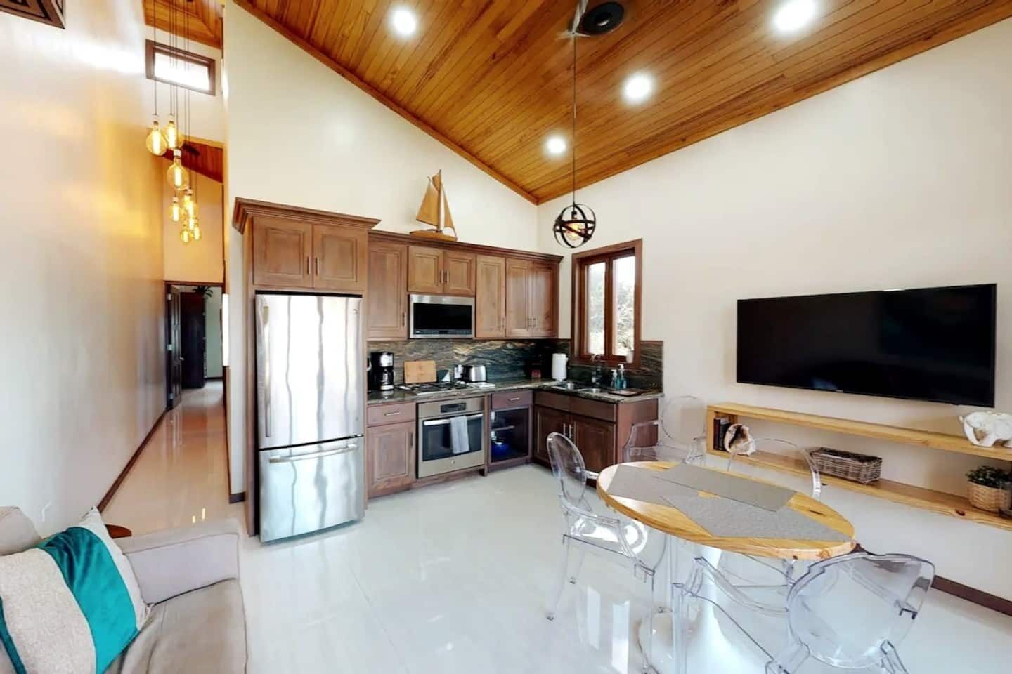 A modern kitchen with wooden cabinets, stainless steel appliances, and a large flat-screen TV.