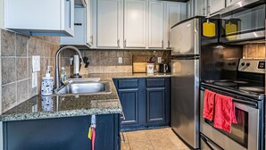 Una cocina moderna con gabinetes blancos, encimera de granito, electrodomésticos de acero inoxidable y una pequeña isla con fregadero.