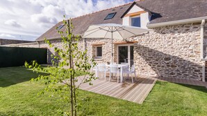 Una casa de piedra con terraza de madera, un patio con mobiliario exterior y un pequeño jardín.
