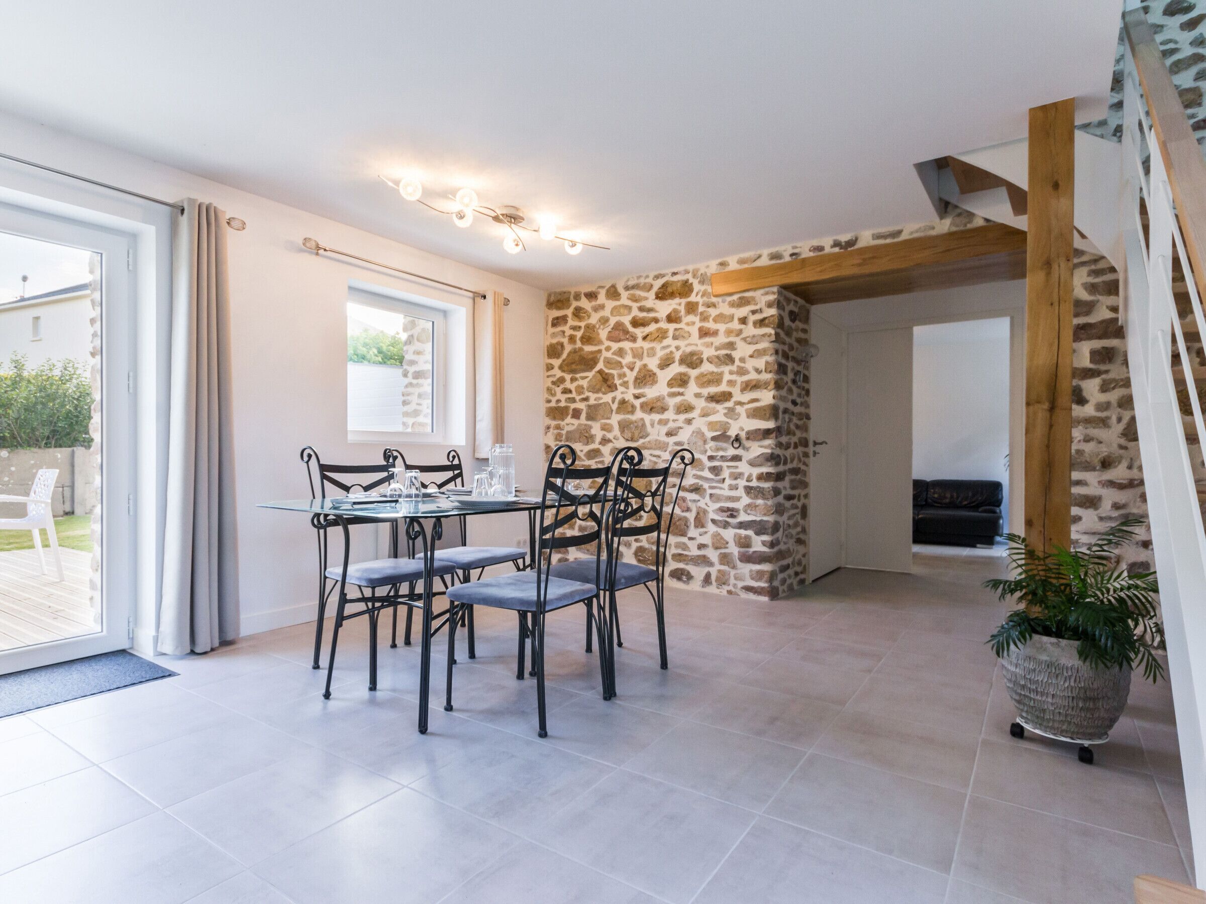 A dining area with a table set for four, a stone wall, and a staircase leading to another level.