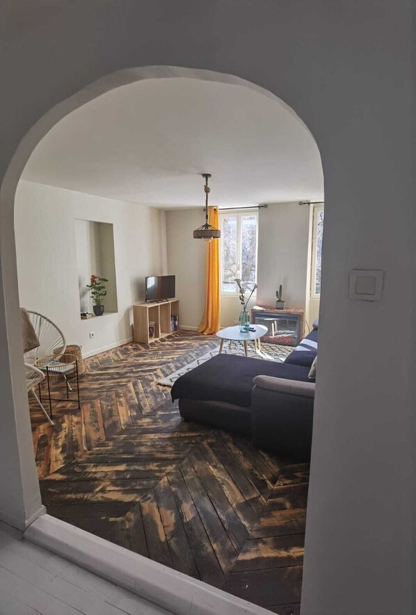 A living room with a herringbone floor, a sofa, a TV, and a window with curtains.