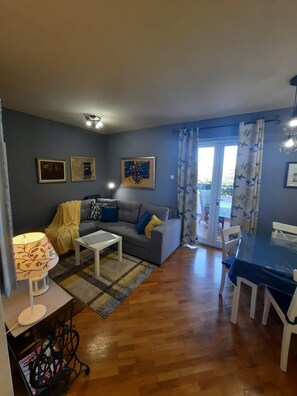 A living room with a sofa, coffee table, and dining table. There are curtains, a lamp, and wall art. - Premium apartment Sunny (Porec)