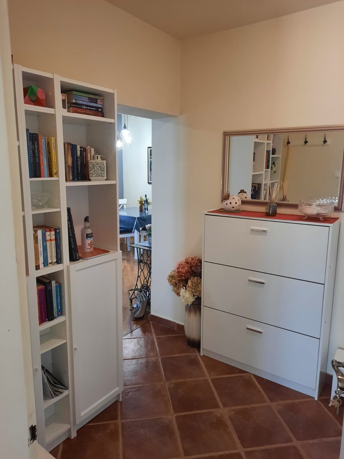 A room with a white wardrobe, a mirror, and a bookshelf with books.