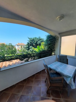 Un balcon avec une table et des chaises, une vue sur la verdure et les bâtiments, et un sol carrelé.