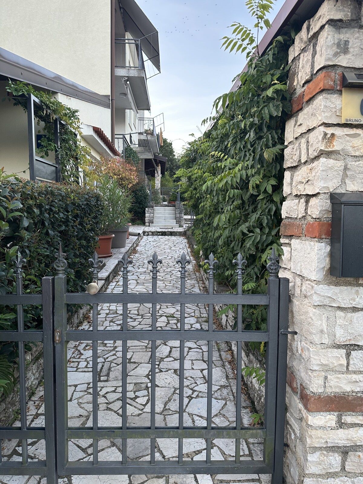 Una entrada con reja y un sendero de piedra que lleva a un edificio con fachada de piedra y portón metálico.