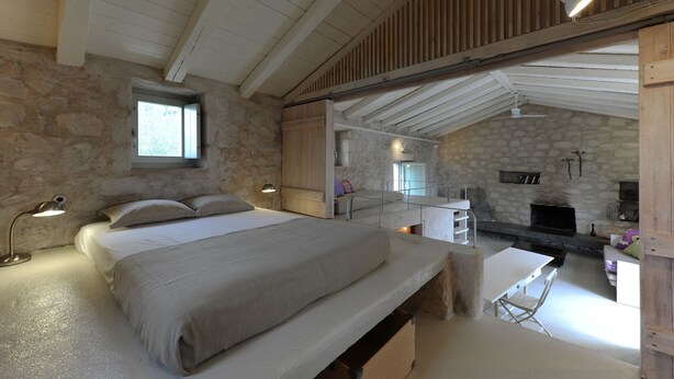 Une chambre avec un grand lit, un bureau et un mur en pierre.
