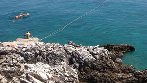 Un rivage rocheux bordé d’une eau d’un bleu limpide, un petit bateau ancré près du rivage et une montagne lointaine.