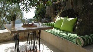 Un espace extérieur ensoleillé, aménagé avec une table, des coussins et une plante en pot.