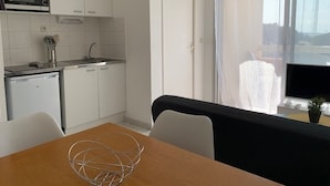 A compact kitchen with white cabinets, a microwave, and a small refrigerator. There is a dining area with a table and chairs, and a large window with a view of the outside. - 2* Apt with AC and Pets Allowed in Balaruc-les-Bains (Balaruc-les-Bains)