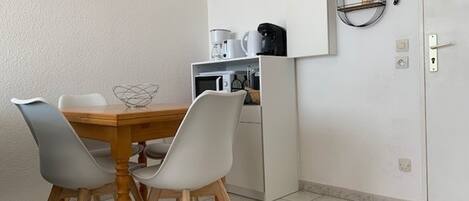 Een kleine keuken met een magnetron, koffiezetapparaat en een kleine koelkast. Er is een eettafel met twee stoelen en een decoratieve schaal.