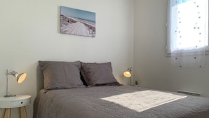 A bedroom with a bed, two bedside lamps, a nightstand, a wall-mounted picture, and a window with blinds. - 2* Apt with AC and Pets Allowed in Balaruc-les-Bains (Balaruc-les-Bains)