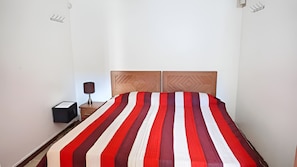 Una cama con colcha a rayas, cabecera de madera, mesita de noche con lámpara y una pequeña caja.