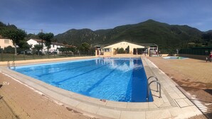 Una piscina con agua cristalina azul, rodeada por una solana de ladrillo y una zona vallada.