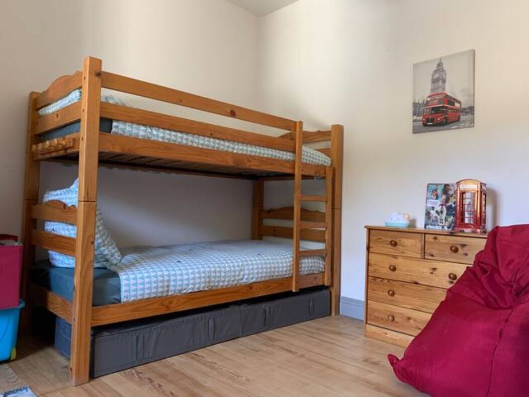 A bunk bed with a wooden frame, a dresser with drawers, and a framed picture on the wall.