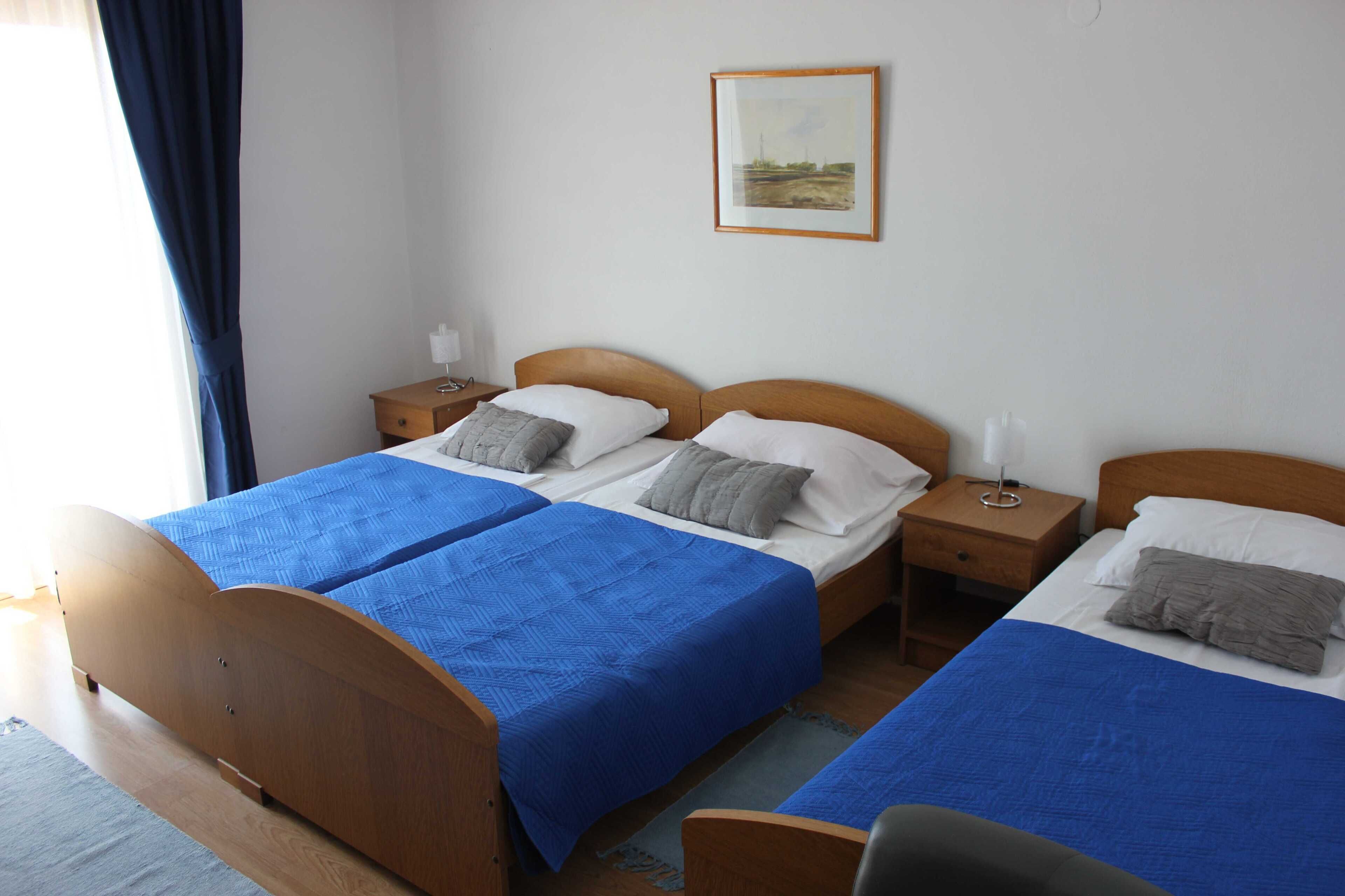 A double room with two beds, each with a blue bedspread, wooden headboards, and bedside tables with lamps.