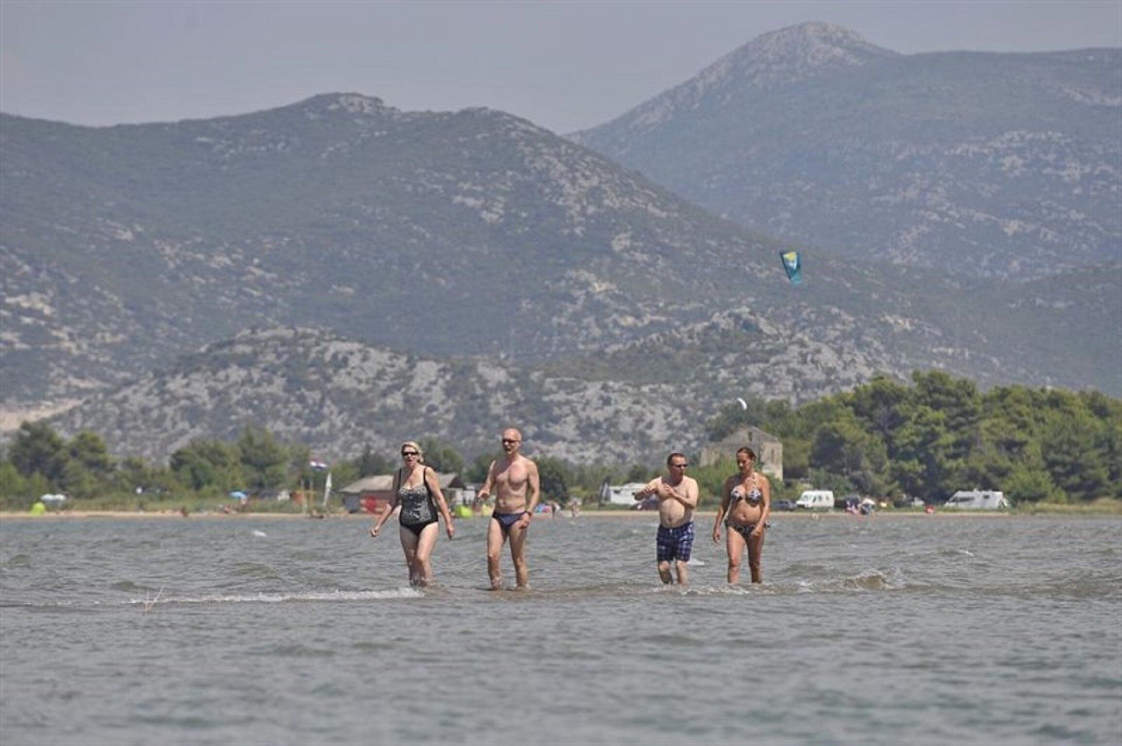 Un grupo de personas caminando en aguas poco profundas cerca de una playa con montañas al fondo.