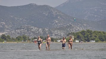 Un grupo de personas caminando en aguas poco profundas cerca de una playa con montañas al fondo.