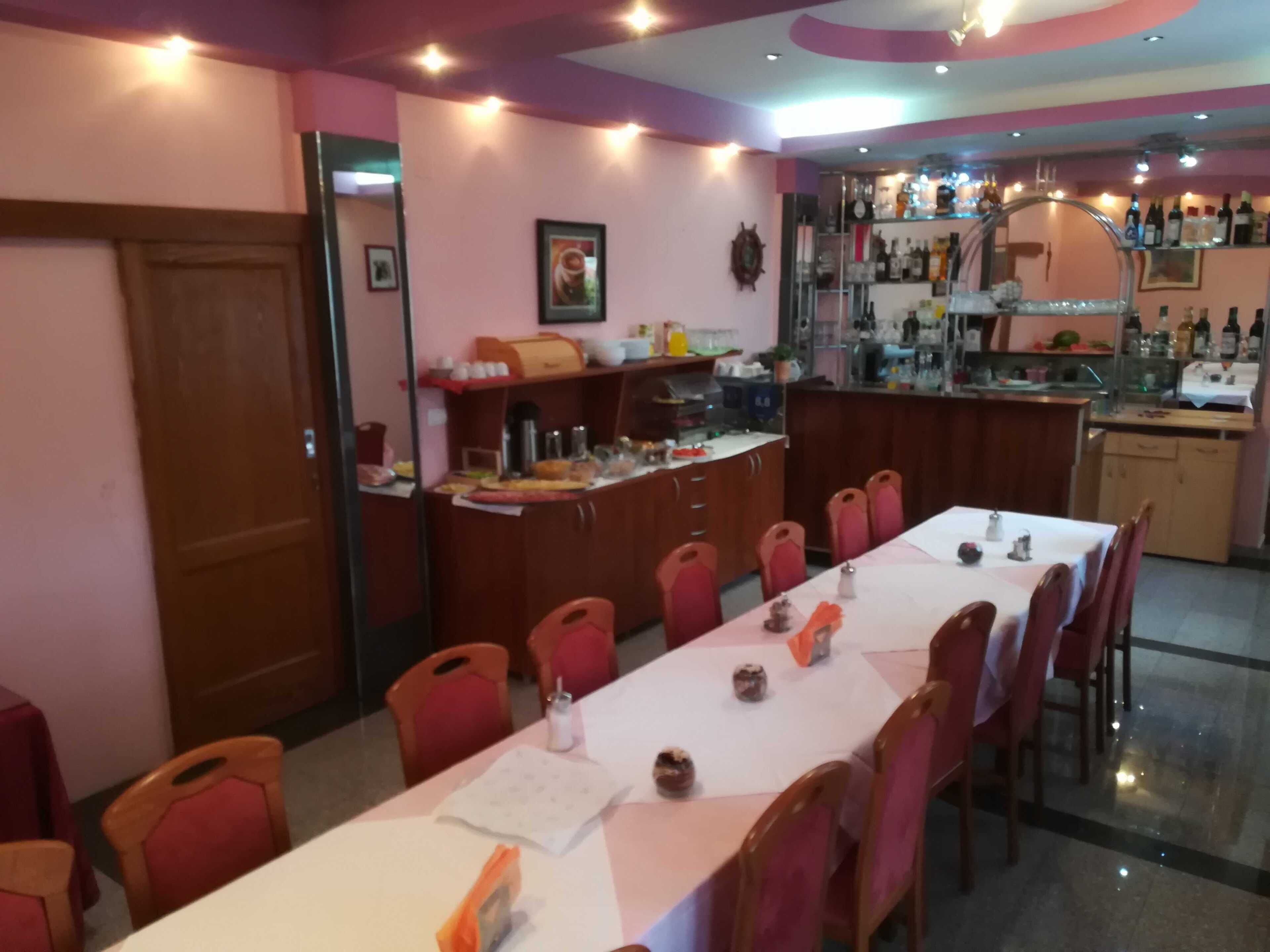 Zona pranzo con un tavolo lungo, sedie rosse, angolo cottura con bancone e diversi elettrodomestici.