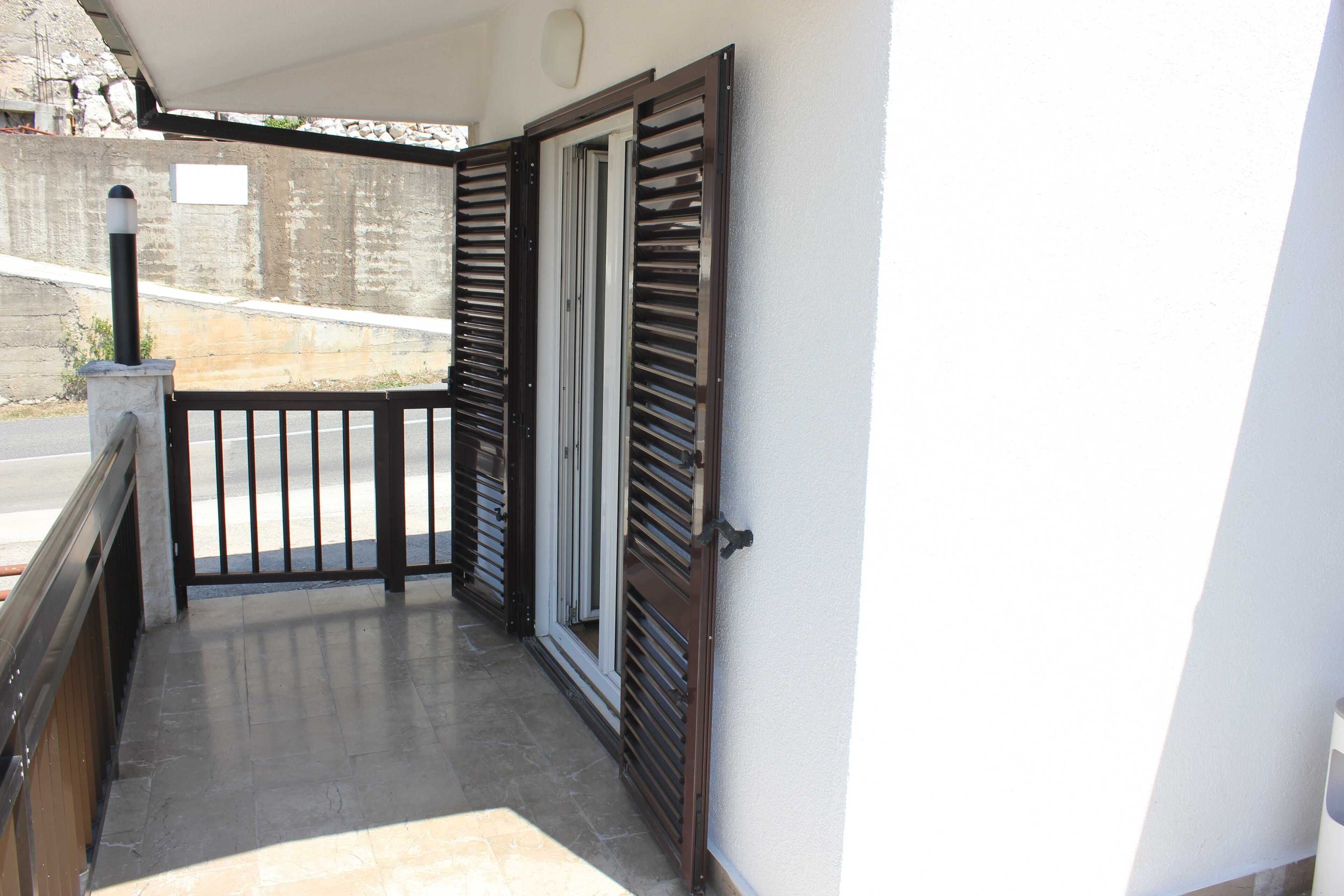 A balcony with a metal gate, a concrete wall, and a tiled floor.