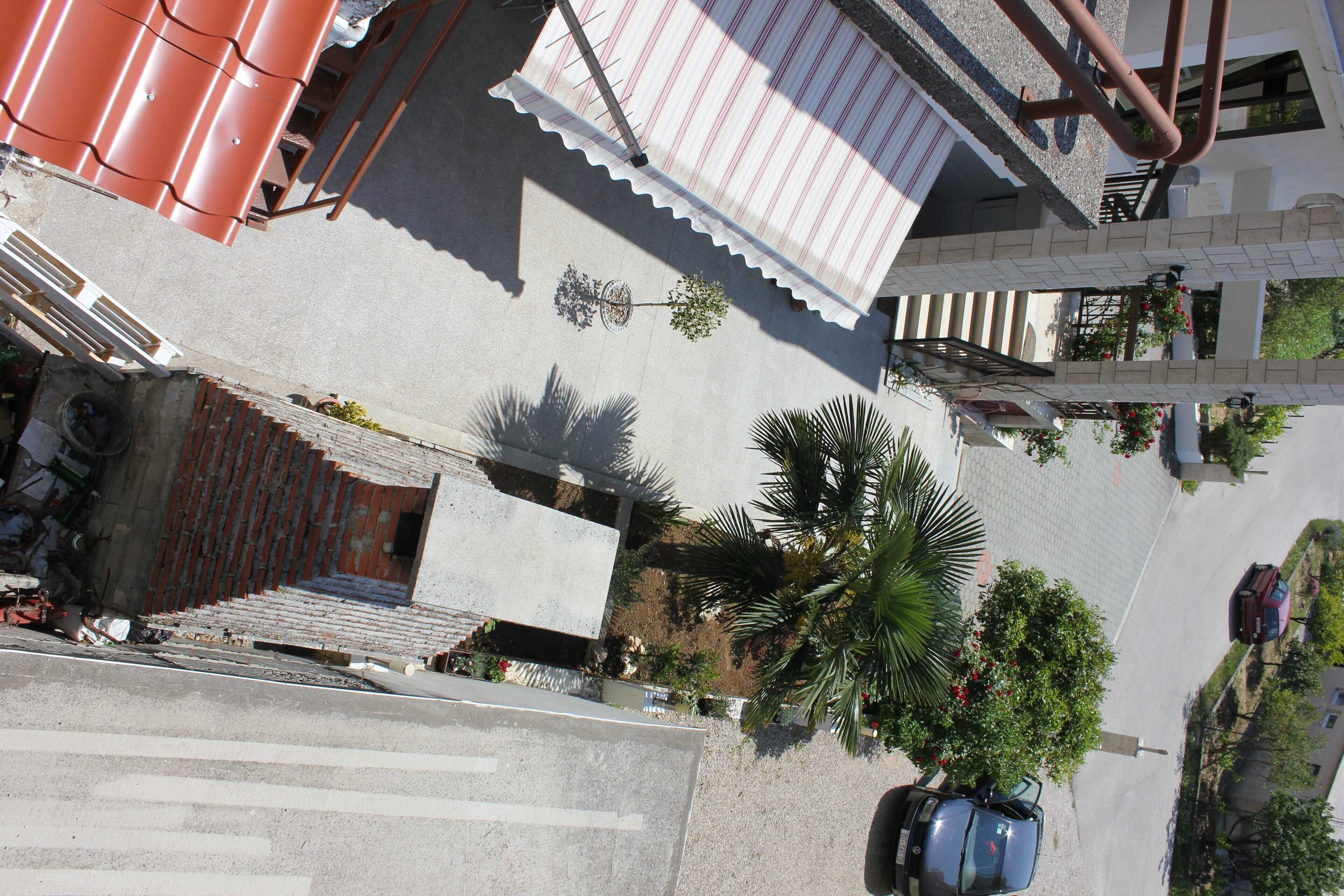 A street view with a building featuring a red roof, a staircase, and a parked car.