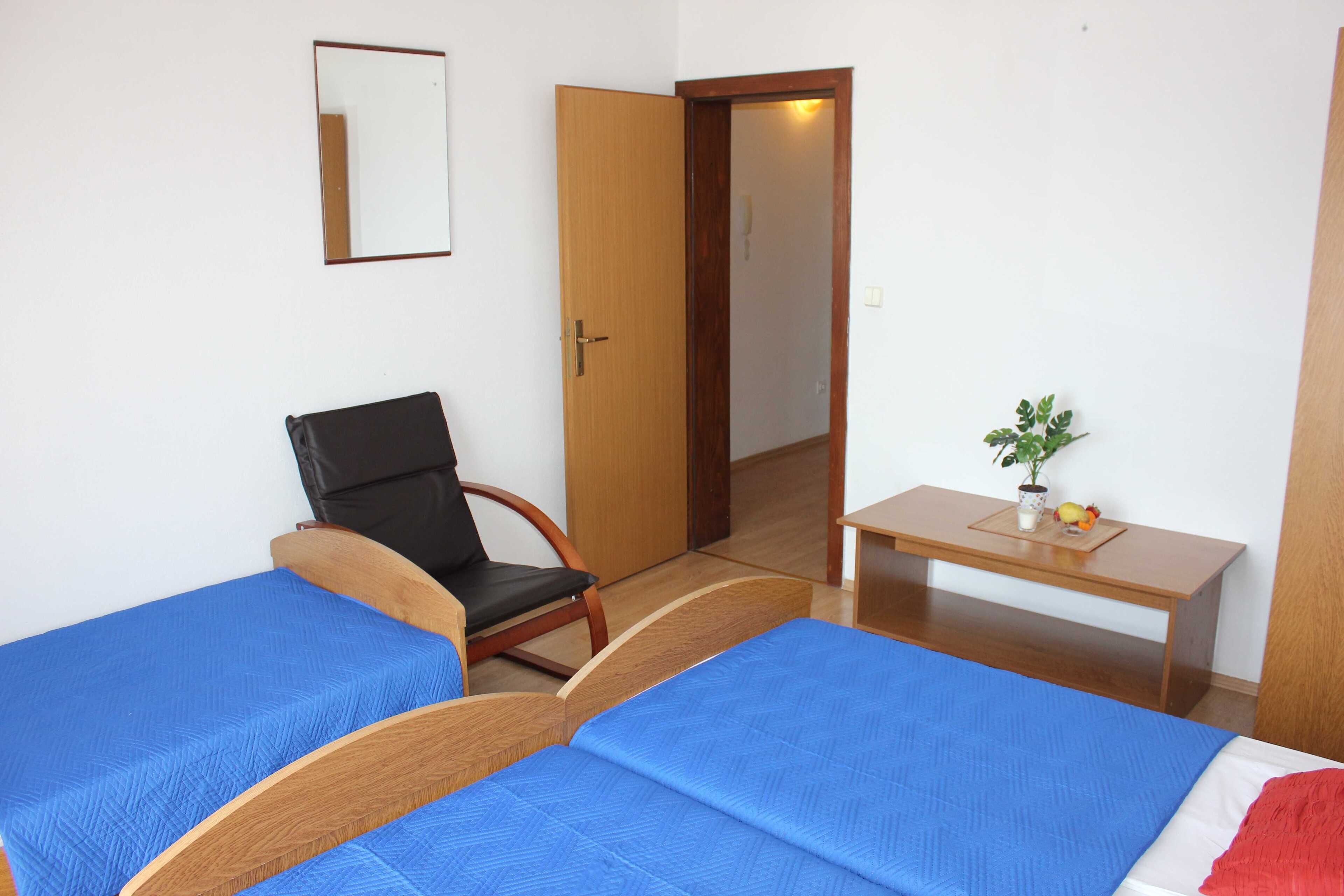 Una habitación con dos camas, una silla, un escritorio, un espejo y una planta pequeña.