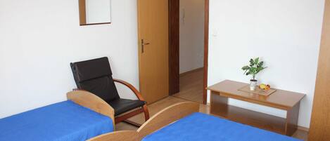 A room with two beds, a chair, a desk, a mirror, and a small plant.
