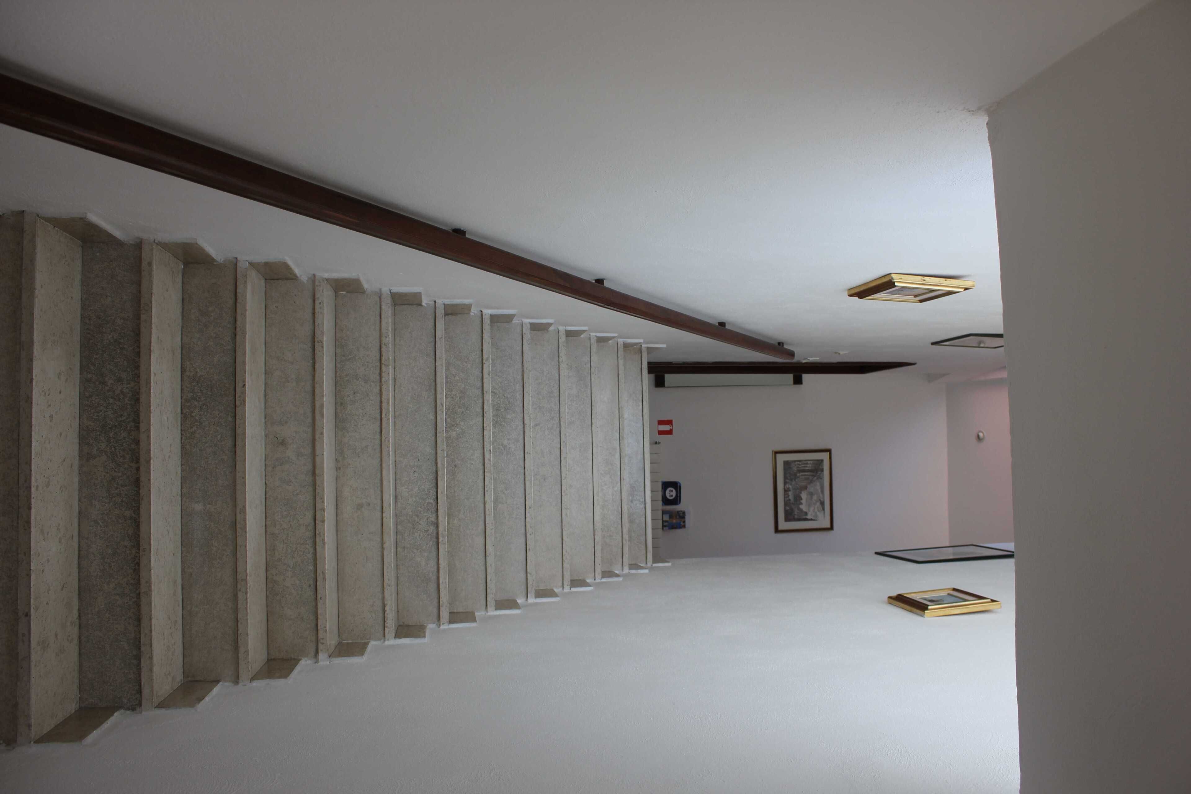 Un pasillo con pared de hormigón, vigas de madera y un cuadro enmarcado en la pared.