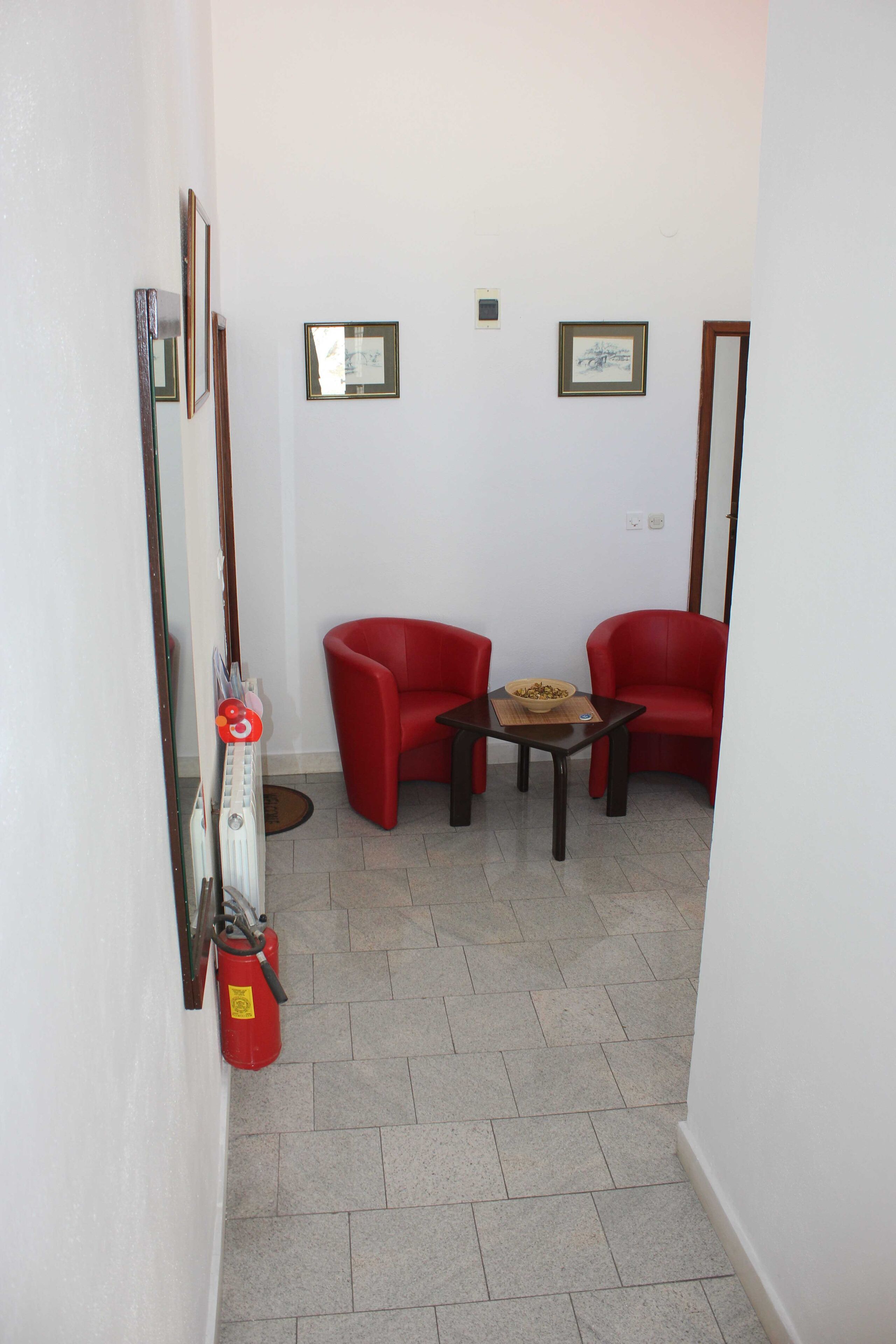 A small room with two red chairs, a table with a bowl, a radiator, and a fire extinguisher.